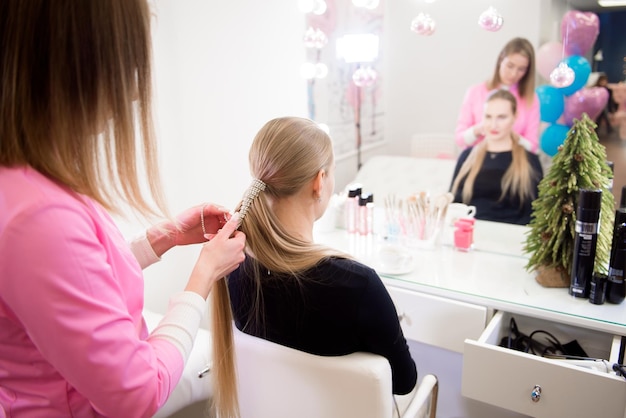 Cabeleireira feminina faz um penteado para uma loira em um salão de beleza