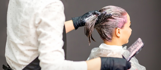 Cabeleireira tingindo o cabelo de jovem caucasiana em salão de cabeleireiro