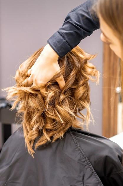 Foto cabeleireira verifica o penteado encaracolado marrom de uma jovem mulher caucasiana no salão de beleza.