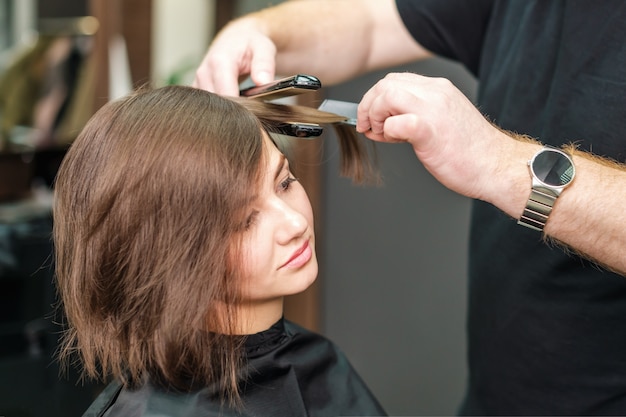 Cabeleireiro alisando cabelos castanhos com ferros de cabelo.