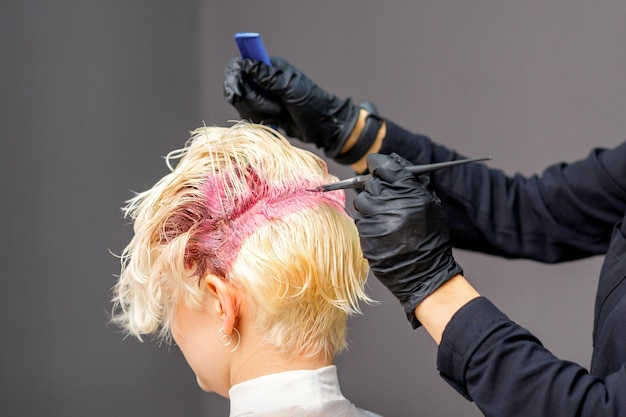 Cabeleireiro colore o cabelo loiro feminino em um salão de beleza.