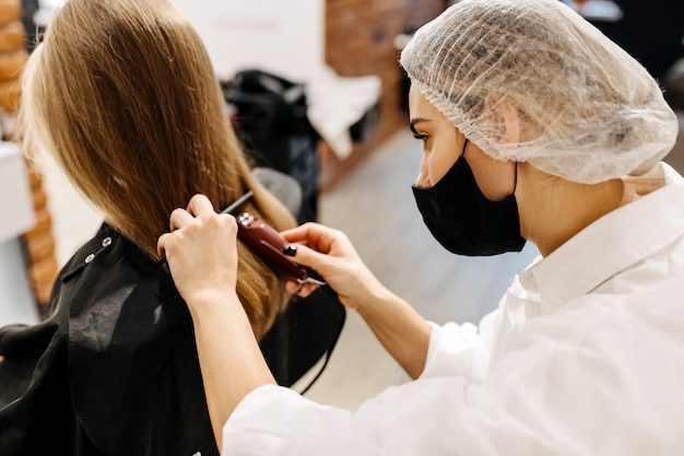 Cabeleireiro com máscara, cortando o cabelo de clientes com uma tesoura de cabelo, em um salão de beleza