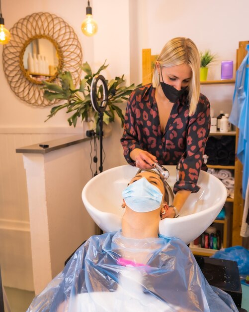 Cabeleireiro com máscara de proteção facial lavando o cabelo do cliente com água e sabão abertura com medidas de segurança de cabeleireiros na pandemia covid19