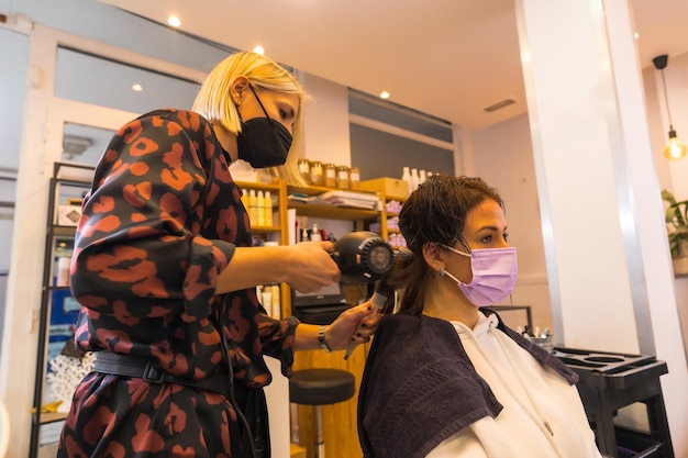 Cabeleireiro com máscara de proteção facial realizando um penteado ao cliente Medidas de segurança na pandemia Covid19 um novo normal