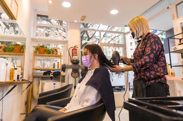 Cabeleireiro com máscara de proteção facial secando o cabelo do cliente com secador de cabelo Medidas de segurança na pandemia Covid19