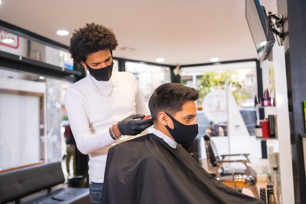 Cabeleireiro com máscara e luvas cortando o cabelo do cliente com navalha