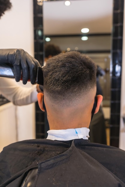 Cabeleireiro com máscara e luvas cortando o cabelo do jovem cliente