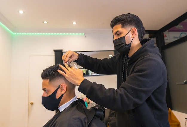 Cabeleireiro com máscara facial cortando o cabelo do jovem cliente