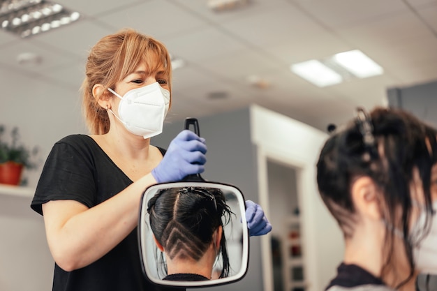 Cabeleireiro com máscara mostrando o resultado do corte no espelho. reabertura com medidas de segurança de cabeleireiros na pandemia de covid-19