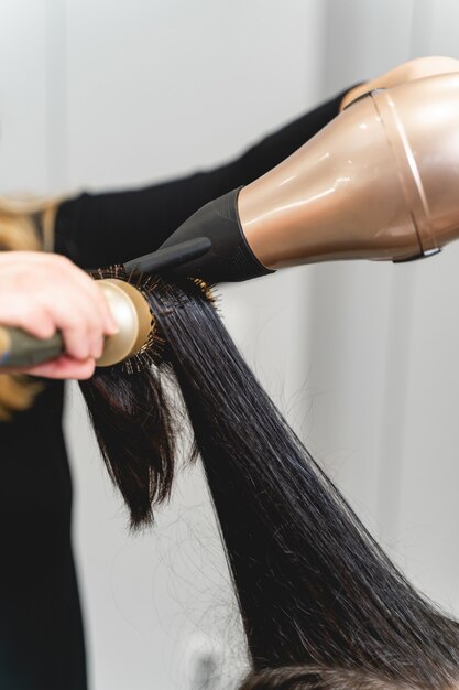 Cabeleireiro competente usando secador de cabelo profissional enquanto faz um novo penteado para sua cliente, fluxo de ar quente