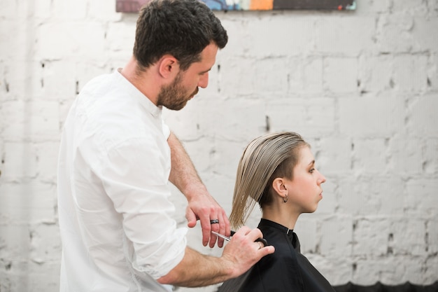 Cabeleireiro corta o cabelo com uma tesoura na coroa do cliente satisfeito bonito no salão de cabeleireiro profissional