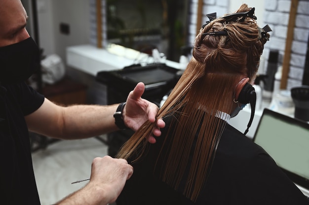 Cabeleireiro corta o cabelo de uma mulher de negócios que se comunica com fones de ouvido em um laptop