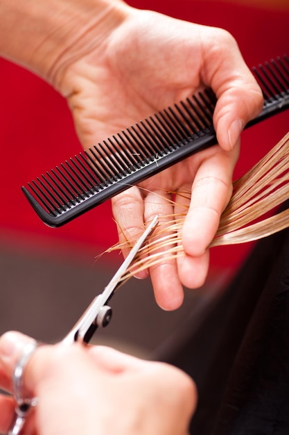 Cabeleireiro corta o cabelo de uma mulher loira/close-up
