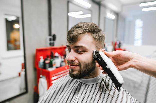 Cabeleireiro corta um homem sorridente com barba usa um aparador