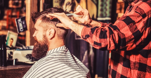 Cabeleireiro cortando o cabelo de um cliente do sexo masculino. Homem visitando cabeleireiro na barbearia. Tesouras de barbeiro. Homem barbudo na barbearia. Trabalho na barbearia. Cabeleireiro de homem.