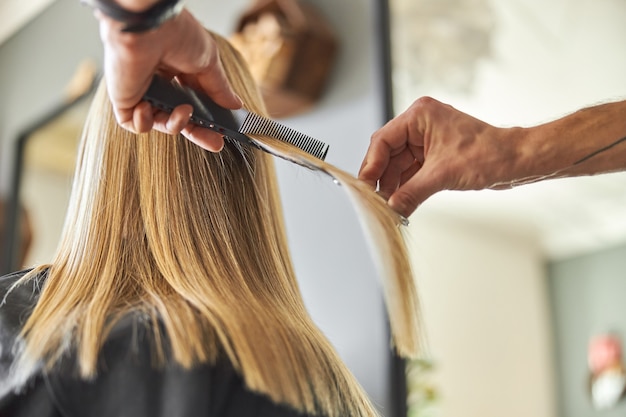 Cabeleireiro cortando o cabelo de uma mulher loira no salão