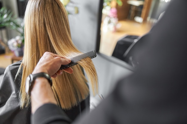 Cabeleireiro cortando o cabelo de uma mulher loira no salão