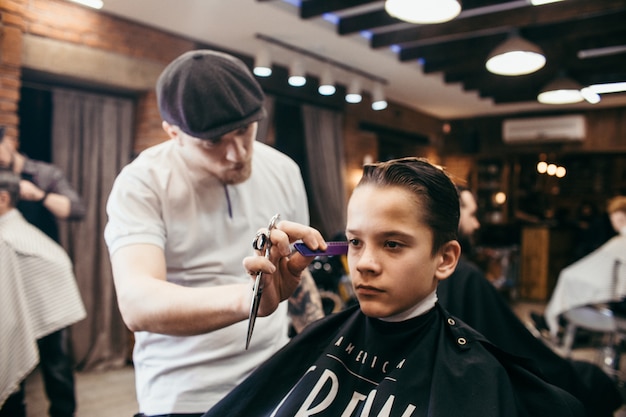 Cabeleireiro de cortes de cabelo de adolescente na barbearia. Penteado retrô elegante na moda