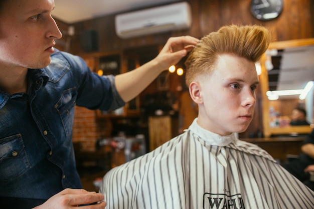 Cabeleireiro de cortes de cabelo de menino ruivo adolescente na barbearia