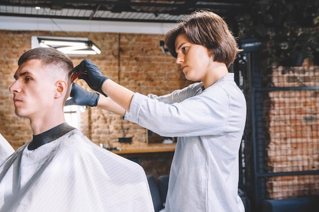 Cabeleireiro de mulher bonita raspa a cabeça da cliente com um aparador elétrico na barbearia. Publicidade e conceito de barbearia