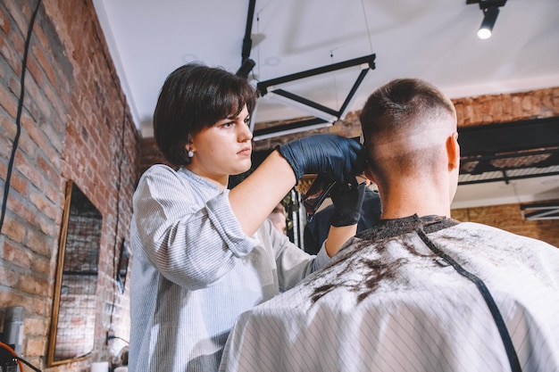 Cabeleireiro de mulher faz um corte de cabelo na cabeça do cliente com um aparador elétrico na barbearia