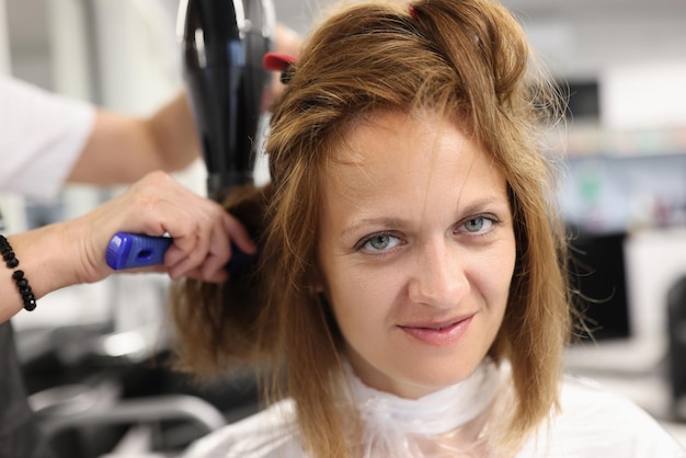 Cabeleireiro de mulher seca e endireita o cabelo do cliente com pente e secador de cabelo no salão de beleza