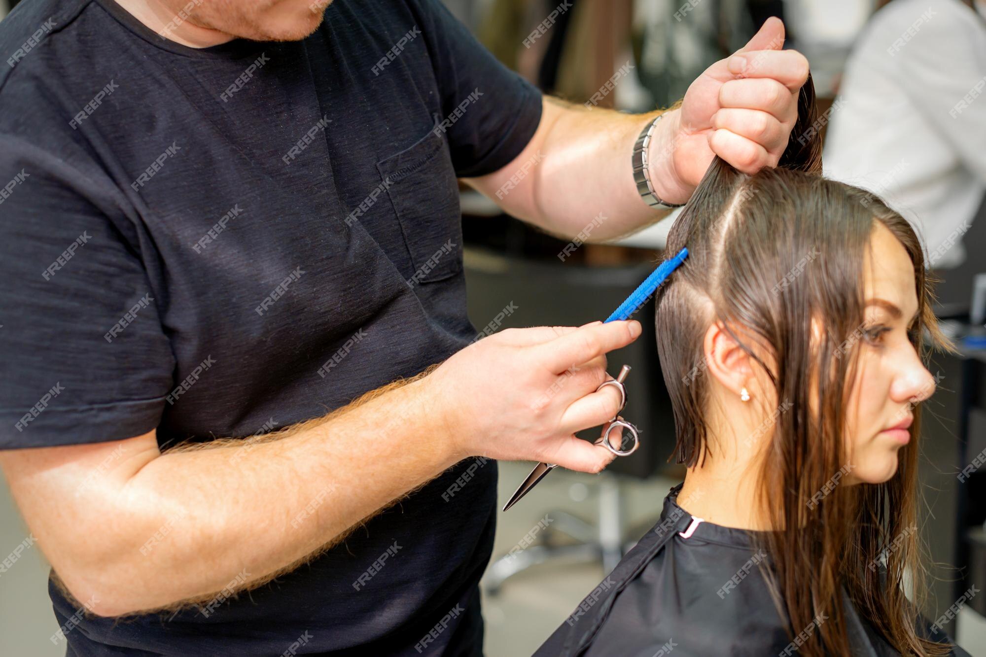 Cabeleireiro divide o cabelo feminino em seções com o pente segurando o  cabelo com as mãos em salão de cabeleireiro close-up.