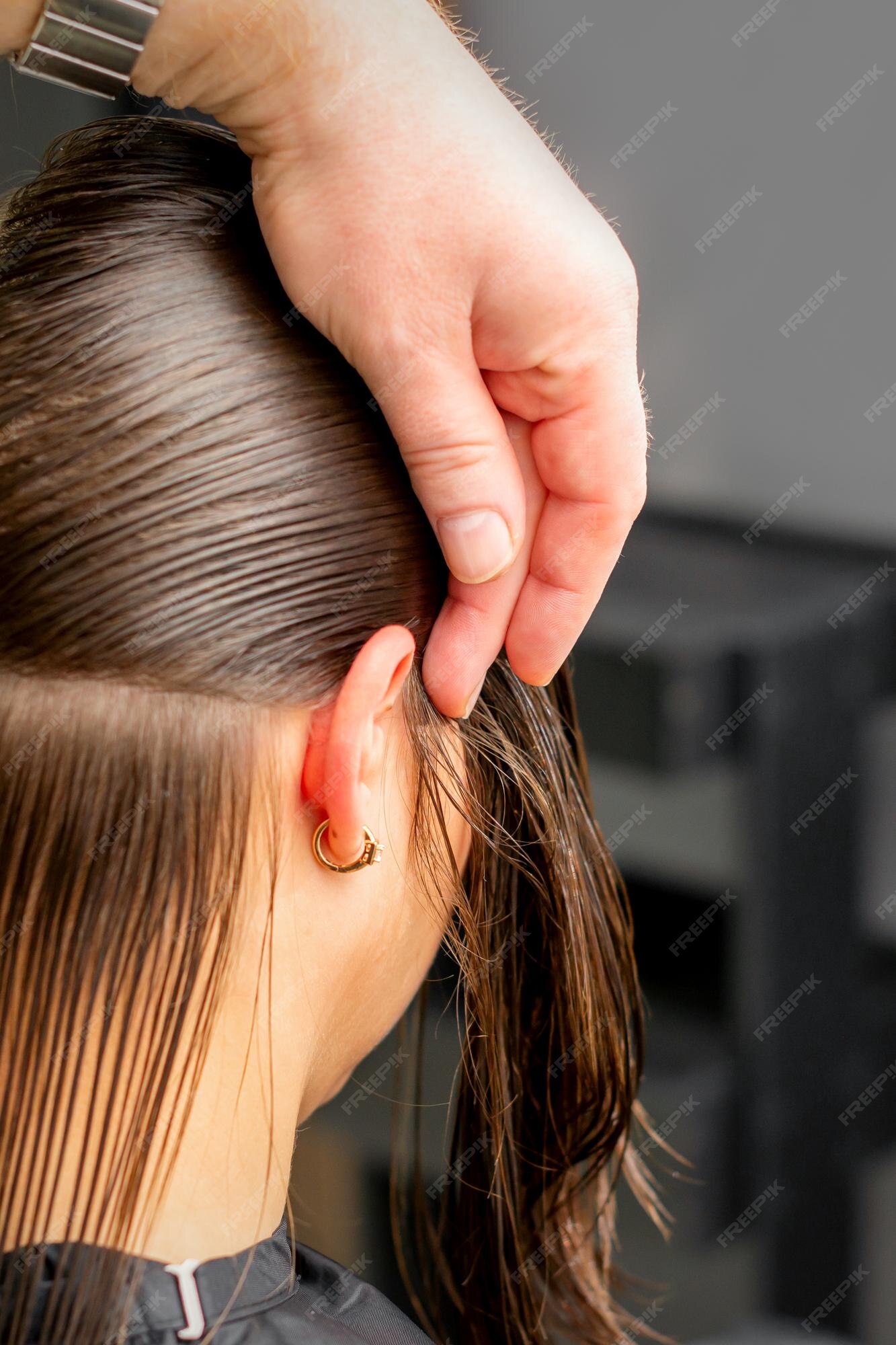 Cabeleireiro divide o cabelo feminino em seções com o pente segurando o  cabelo com as mãos em salão de cabeleireiro close-up.