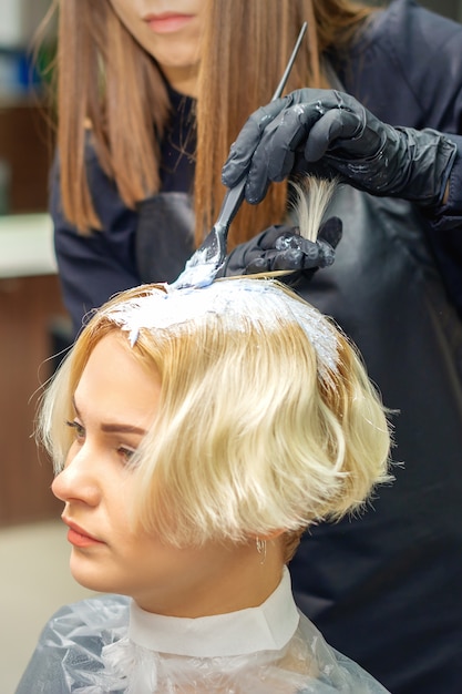 Cabeleireiro em luvas pretas tingindo o cabelo de uma jovem em um salão de cabeleireiro