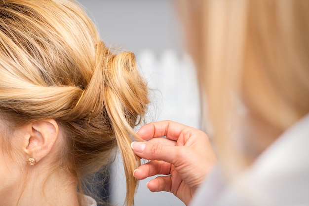 Cabeleireiro em um salão de beleza estilizando o cabelo loiro na parte de trás da cabeça.