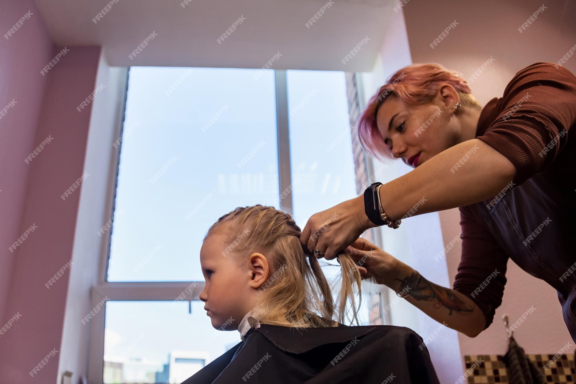 Cabeleireiro de salão de cabeleireiro faz tranças de penteado para bebê  jovem na barbearia mulher de barbeiro faz penteado elegante