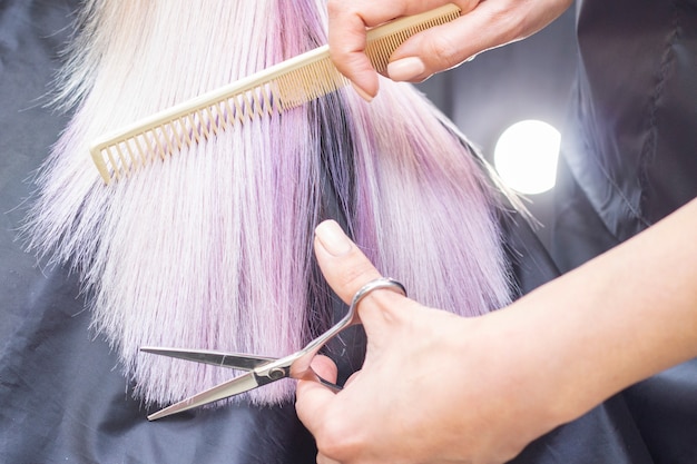 Cabeleireiro faz um corte de cabelo para uma garota com longos cabelos loiros. Cabeleireiro mãos segurando uma tesoura e pente