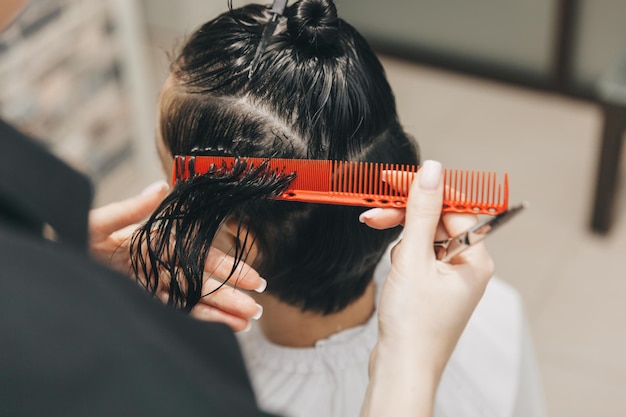 Cabeleireiro faz um corte de cabelo para uma mulher no salão O cabeleireiro corta o cabelo molhado penteando com um pente cliente com vista traseira de cabelo curto