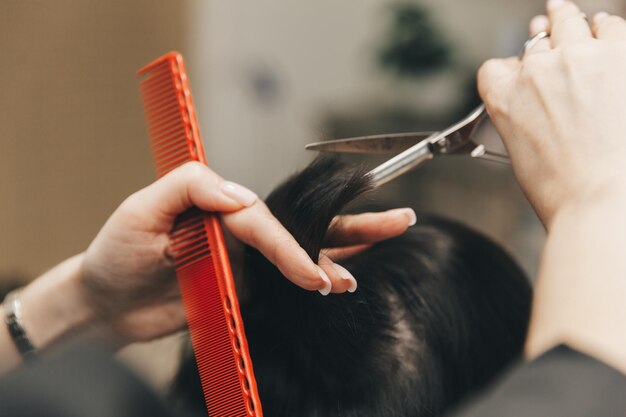 Cabeleireiro faz um corte de cabelo para uma mulher no salão O cabeleireiro corta o cabelo molhado penteando com um pente cliente com vista traseira de cabelo curto