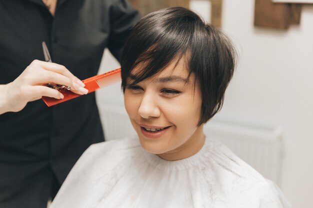 Cabeleireiro faz um corte de cabelo para uma mulher no salão O cabeleireiro corta o cabelo molhado penteando com um pente cliente com vista traseira de cabelo curto