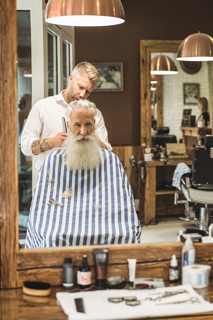 Cabeleireiro fazendo corte de cabelo estiloso para um velho bonito na barbearia