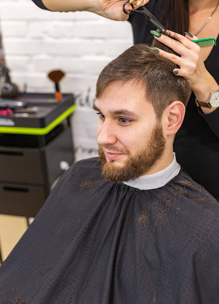 Cabeleireiro fazendo corte de cabelo para cliente do sexo masculino, homem com barba, usando ferramentas profissionais de cabeleireiro