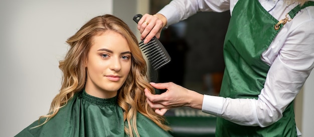 Cabeleireiro fazendo penteado para mulher enquanto penteava com escova de cabelo, penteie em um salão de cabeleireiro.