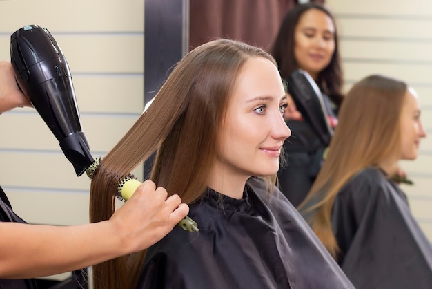 Cabeleireiro feminino, salão de beleza. Secar o cabelo com secador e escova redonda.