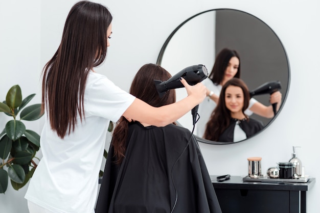 Cabeleireiro focado trabalha secando o cabelo de um cliente bonito