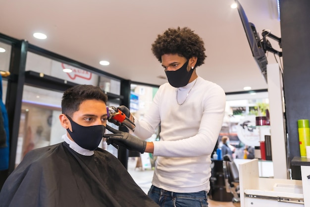 Cabeleireiro latino com máscara e luvas cortando o cabelo do cliente com navalha