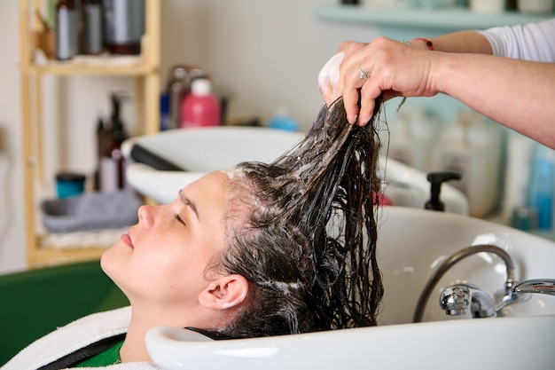 Cabeleireiro lava a cabeça de uma menina morena com shampoo no salão de beleza
