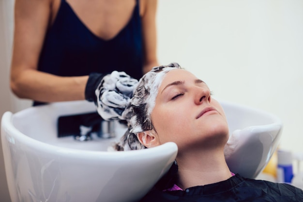 Cabeleireiro lavando o cabelo de uma bela jovem em salão de cabeleireiro.