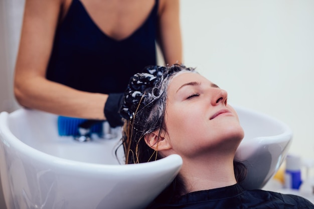 Cabeleireiro lavando o cabelo de uma bela jovem em salão de cabeleireiro.