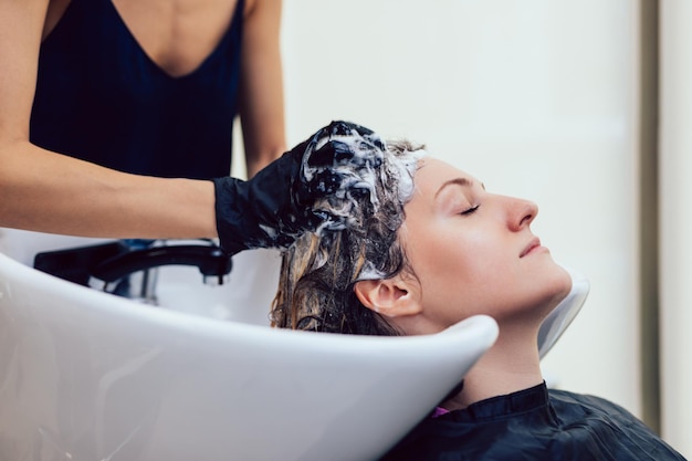 Cabeleireiro lavando o cabelo de uma bela jovem no salão de cabeleireiro.