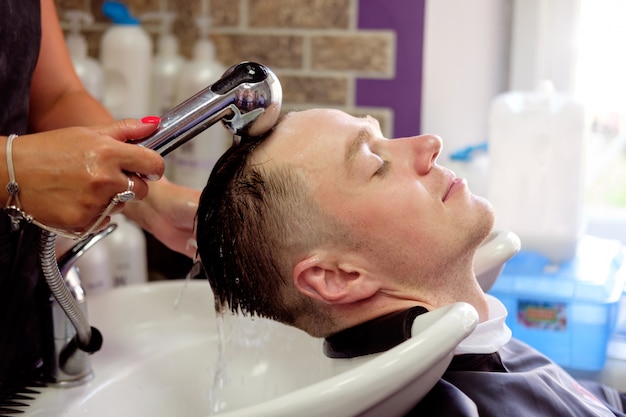 Cabeleireiro, lavando o cabelo para jovem, que tendo prazer e sorrindo