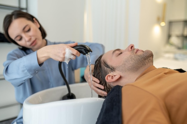 Cabeleireiro lavando o cabelo para o cliente masculino em um salão de beleza