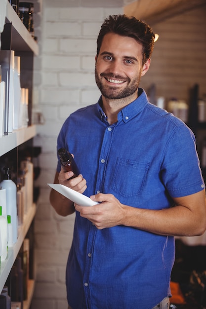 Foto cabeleireiro masculino sorridente, selecionando o xampu da prateleira em um salão de beleza