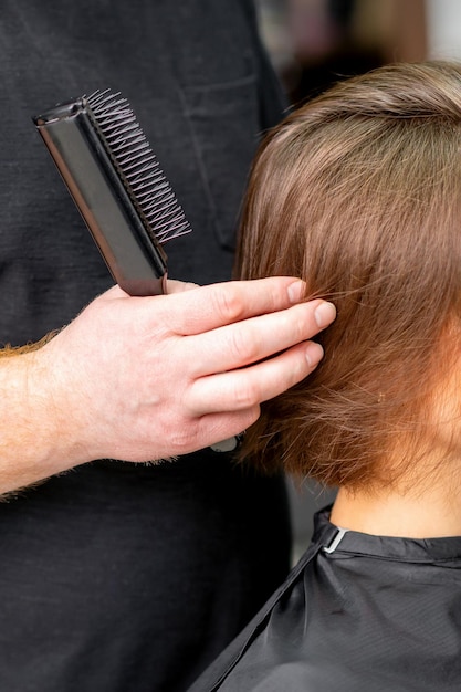 Cabeleireiro masculino trabalha no penteado da jovem mulher morena caucasiana em um salão de cabeleireiro.