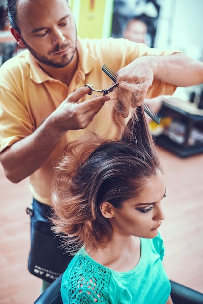 Cabeleireiro masculino trabalhando em um salão de beleza e cortando pontas de cabelo de uma cliente feminina.